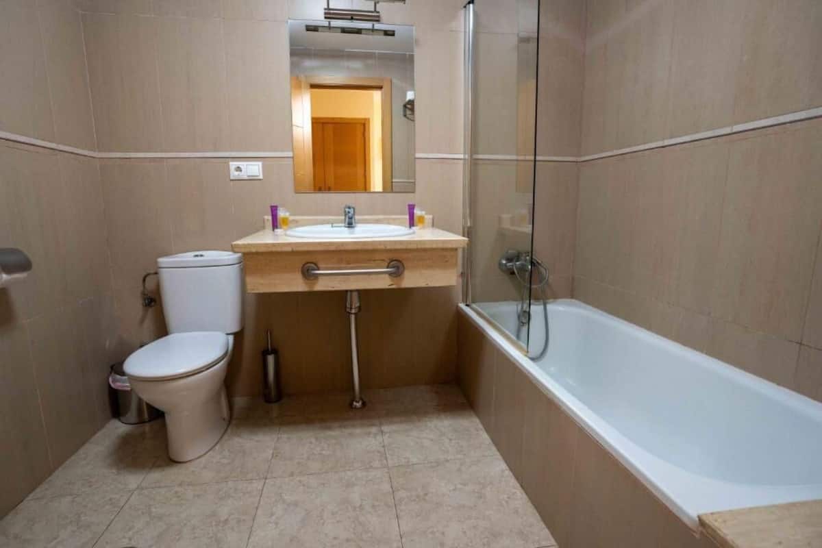 A bathroom with a toilet, sink, mirror, and bathtub.