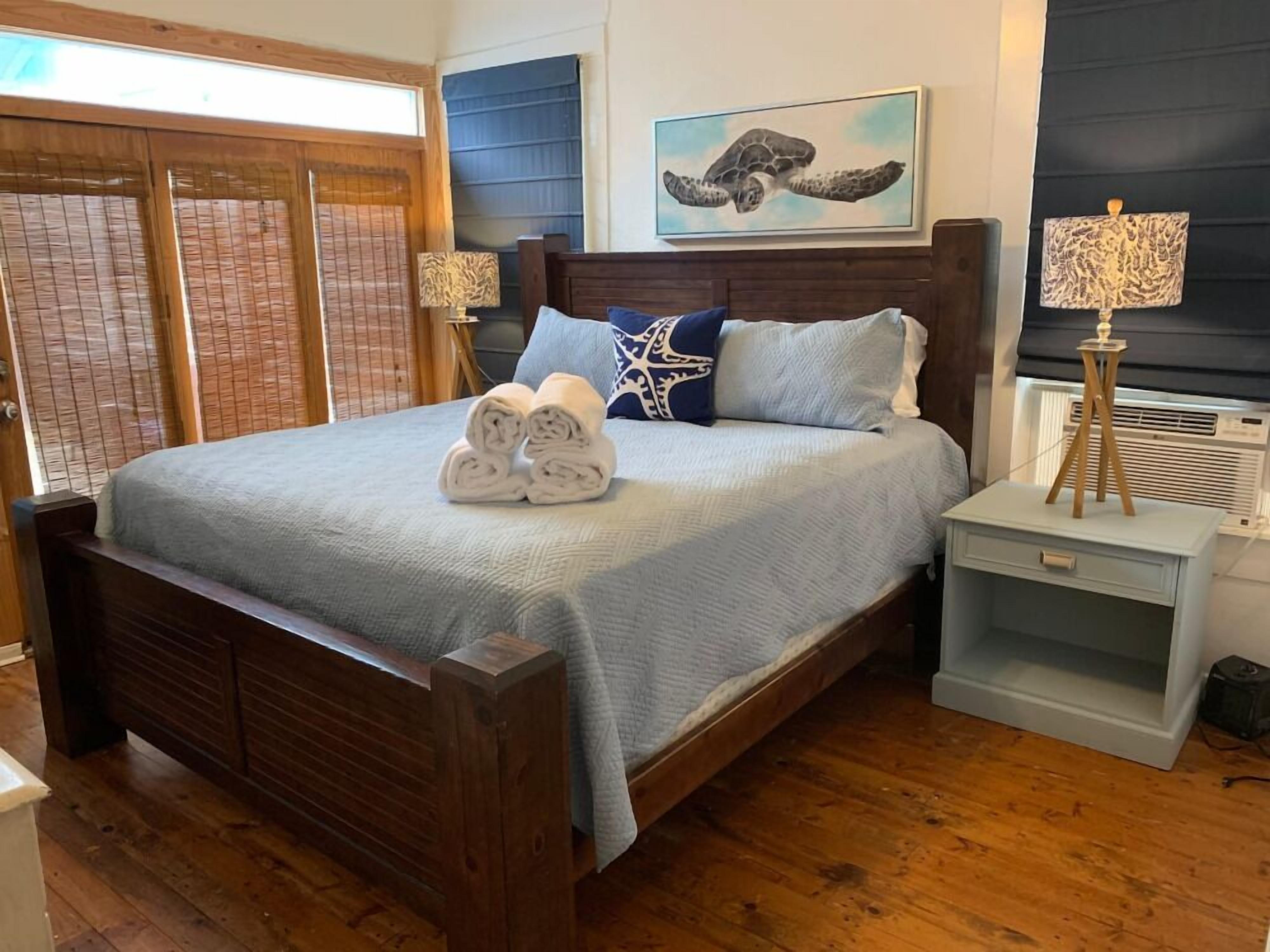 Un dormitorio con una cama de madera, una mesita de noche con lámpara, una ventana con persianas y un aire acondicionado instalado en la pared.
