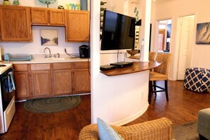 A kitchen with wooden cabinets, a built-in TV, and a dining area with wicker chairs. - 2423 Q5 Near the Pier (Galveston)