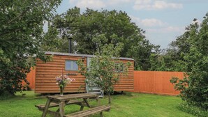 A wooden cabin with a nameplate, a picnic table, and a fenced yard. - Bramleys (Watchet)
