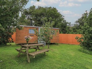 A wooden cabin with a nameplate, a picnic table, and a fenced yard. - Bramleys (Watchet)