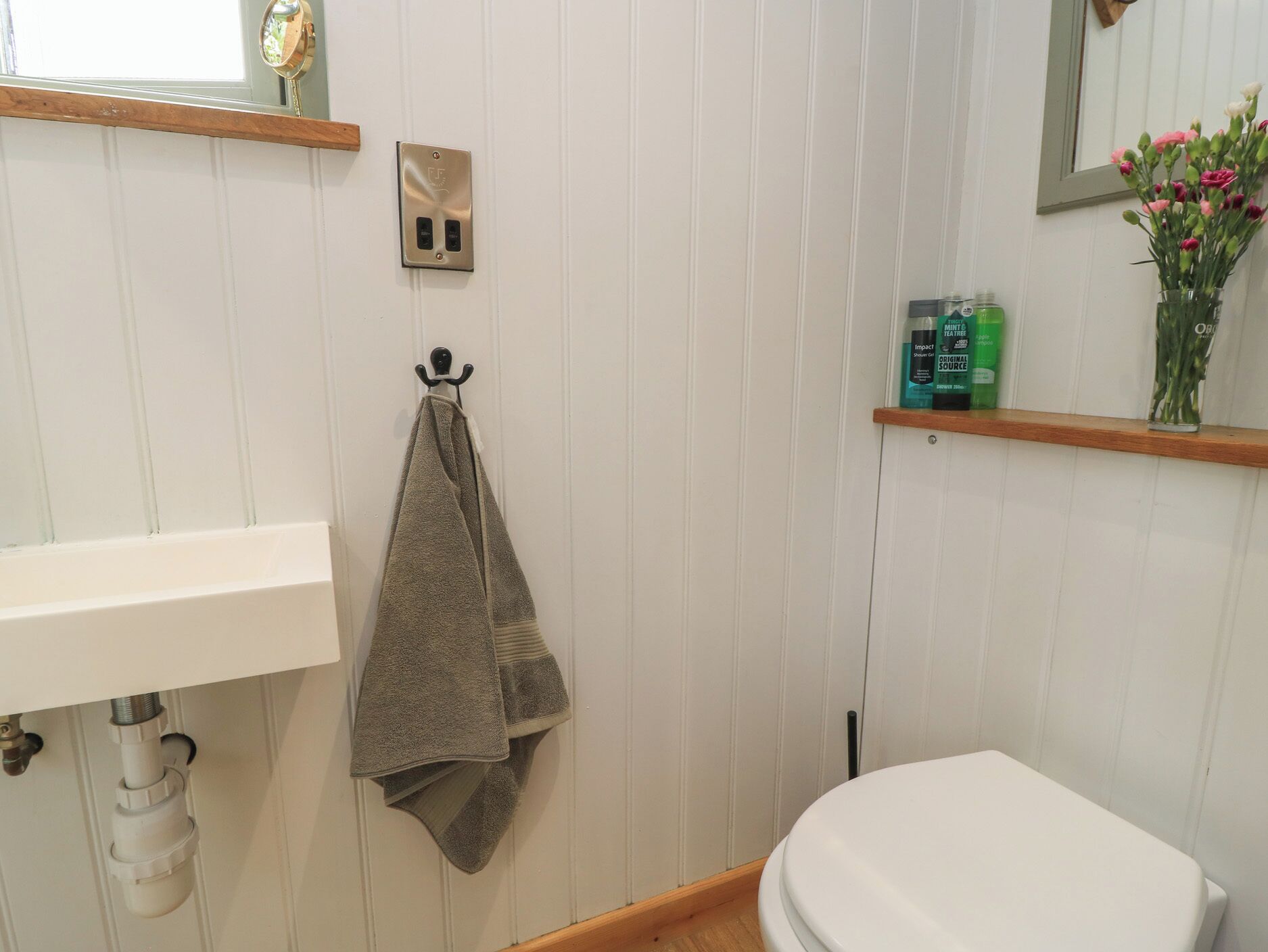 A bathroom with a white sink, a towel hanging on a hook, a toilet, and a shelf with toiletries.