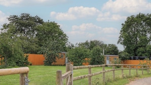 A rural setting with a wooden fence, a gravel path, and two wooden cabins with attached structures. - Bramleys (Watchet)