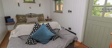 Un dormitorio con una cama, dos ventanas, una puerta y una pequeña estantería con una botella.