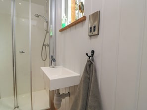 A bathroom with a glass shower enclosure, a white sink, a towel rack, and a wooden shelf.