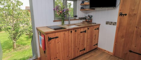 Una cocina con encimera de madera, una ventana con un florero, un televisor montado y una puerta.