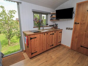 A kitchen with a wooden countertop, a window with a flower vase, a mounted TV, and a door. - Bramleys (Watchet)