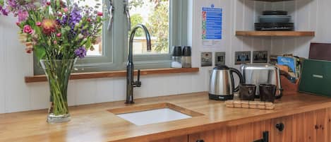 A kitchen with a wooden countertop, a sink, a kettle, and a vase of flowers.