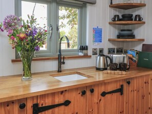 A kitchen with a wooden countertop, a sink, a kettle, and a vase of flowers. - Bramleys (Watchet)