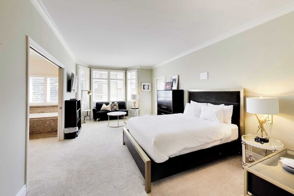A hotel room with a bed, a desk, a chair, a TV, and a window with blinds.