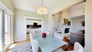 Un comedor con una mesa de vidrio, sillas blancas con diseño, una araña y una chimenea.