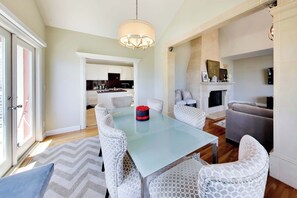 Un coin repas avec une table en verre, des chaises blanches à motifs, un lustre et une cheminée.