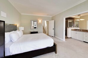 Une chambre à coucher comprenant un lit, une table de chevet, une lampe, un miroir, une porte et une salle de bain avec un lavabo et un miroir.