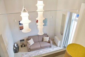 Een moderne woonkamer met een bank, een glazen salontafel en hanglampen.