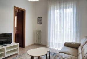 A living room with a sofa, a TV on a stand, a small table, a door, and a radiator. - Bright Nest Bande Nere – Milano Apartment (Milano)