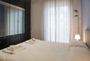 A hotel room with a bed, a mirror, a lamp, and a window with curtains. - Bright Nest Bande Nere – Milano Apartment (Milano)