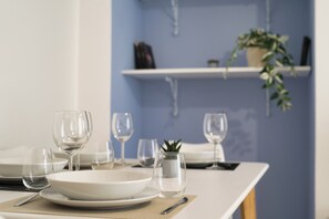 A dining table set with plates, glasses, and cutlery, a small potted plant, and a shelf with decorative items in a room with blue walls. - Bright Nest Bande Nere – Milano Apartment (Milano)