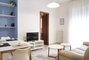 A modern living room with a TV, sofa, coffee table, and a dining area with chairs and a table. - Bright Nest Bande Nere – Milano Apartment (Milano)