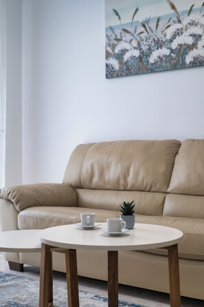 A beige sofa with a small potted plant and two white cups on a round table. - Bright Nest Bande Nere – Milano Apartment (Milano)