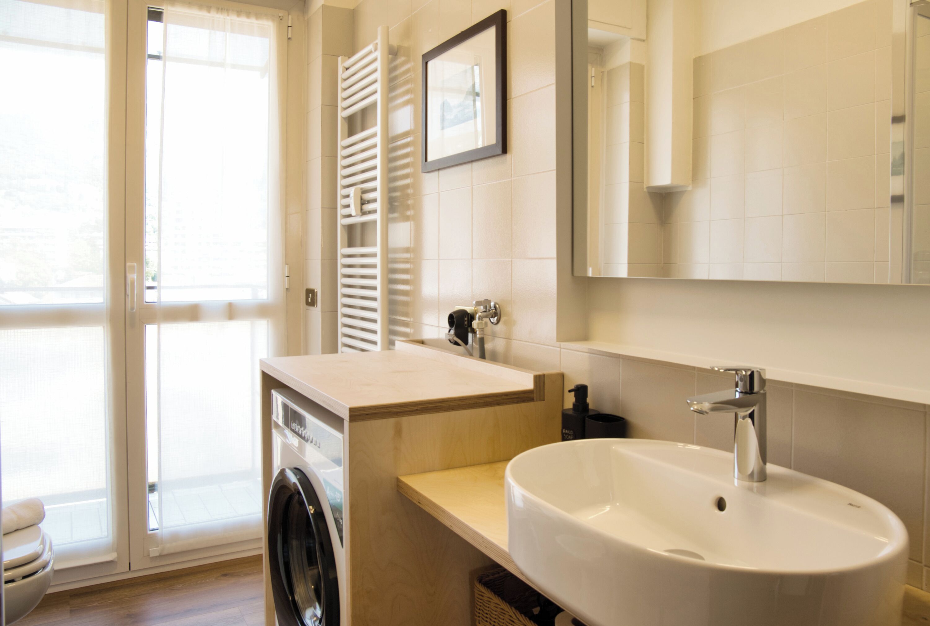 A modern bathroom with a washing machine, a sink, and a large mirror.