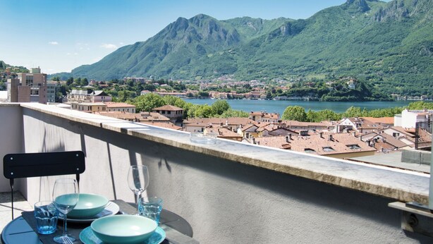 A balcony with a table set for dining, overlooking a town and mountains.
