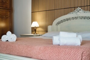 Una cama bien hecha con toallas enrolladas, una lámpara de noche y un cabecero de madera.