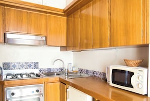Een keuken met houten kastjes, een gasfornuis, een magnetron en een spoelbak.