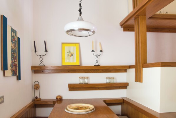 Un comedor con una mesa de madera, un reloj y estantes en la pared con objetos decorativos.