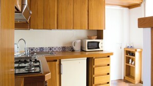 Una cocina con armarios de madera, microondas, refrigerador pequeño y estufa a gas.