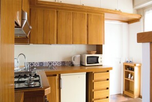 Een keuken met houten kastjes, een magnetron, een kleine koelkast en een gasfornuis.