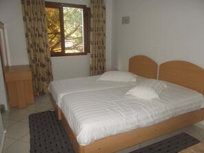 Ein Einzelbett mit Holz Kopfteil, ein Nachttisch und ein Fenster mit Vorhängen.
