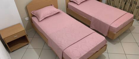 Two single beds with wooden headboards, a small bedside table with a remote control, and a curtain on the right side.