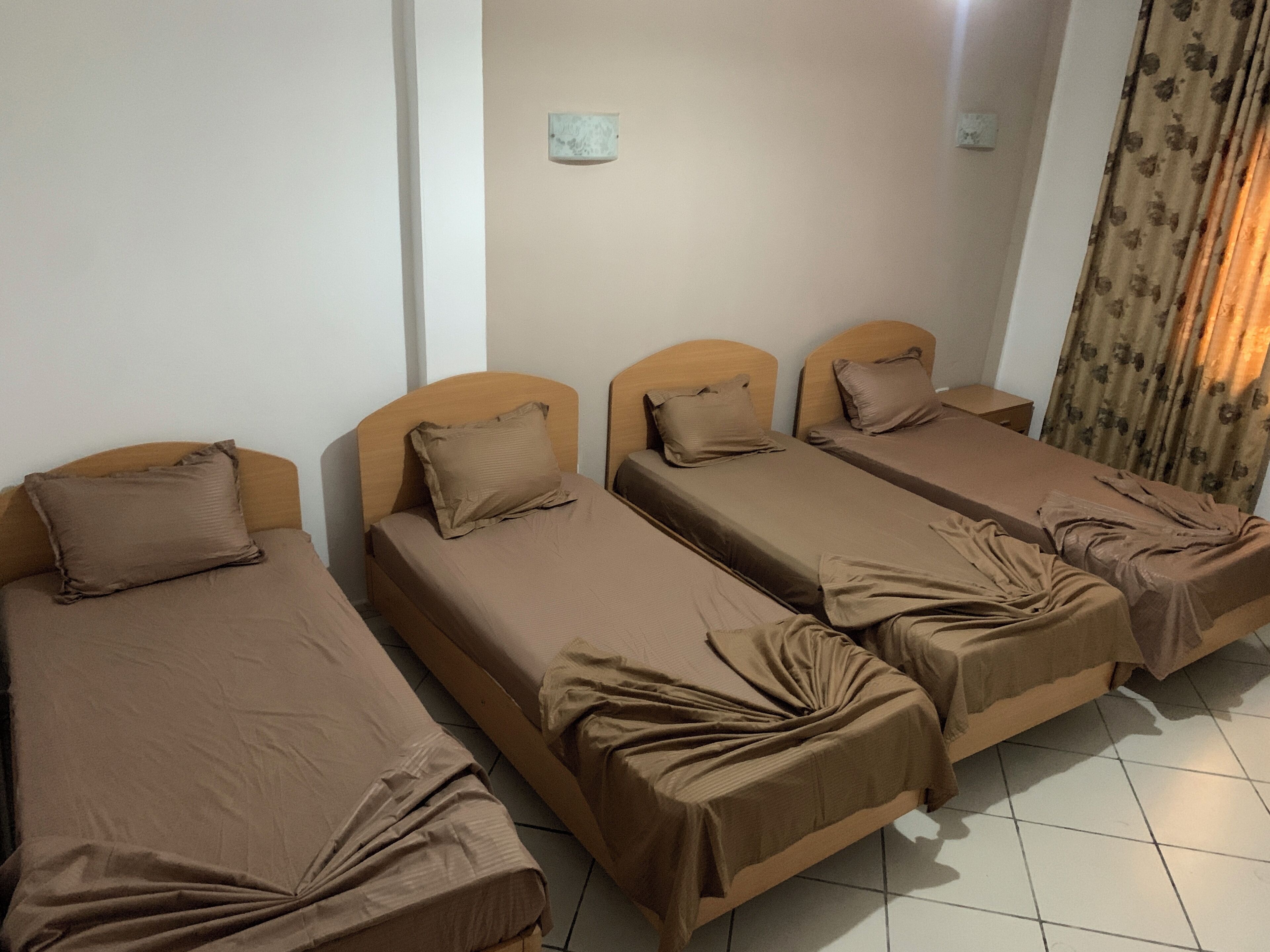 Ein Zimmer mit vier Einzelbetten, jedes mit Kopfstütze und Kissen. Die Betten sind mit braunen Laken bezogen.