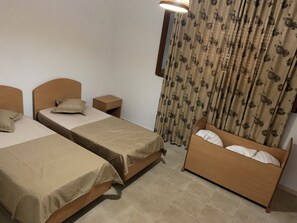 A hotel room with two single beds, a nightstand, a wooden headboard, a curtain with a floral pattern, and a wall-mounted lamp. - Montazah Residence (Bizerte)