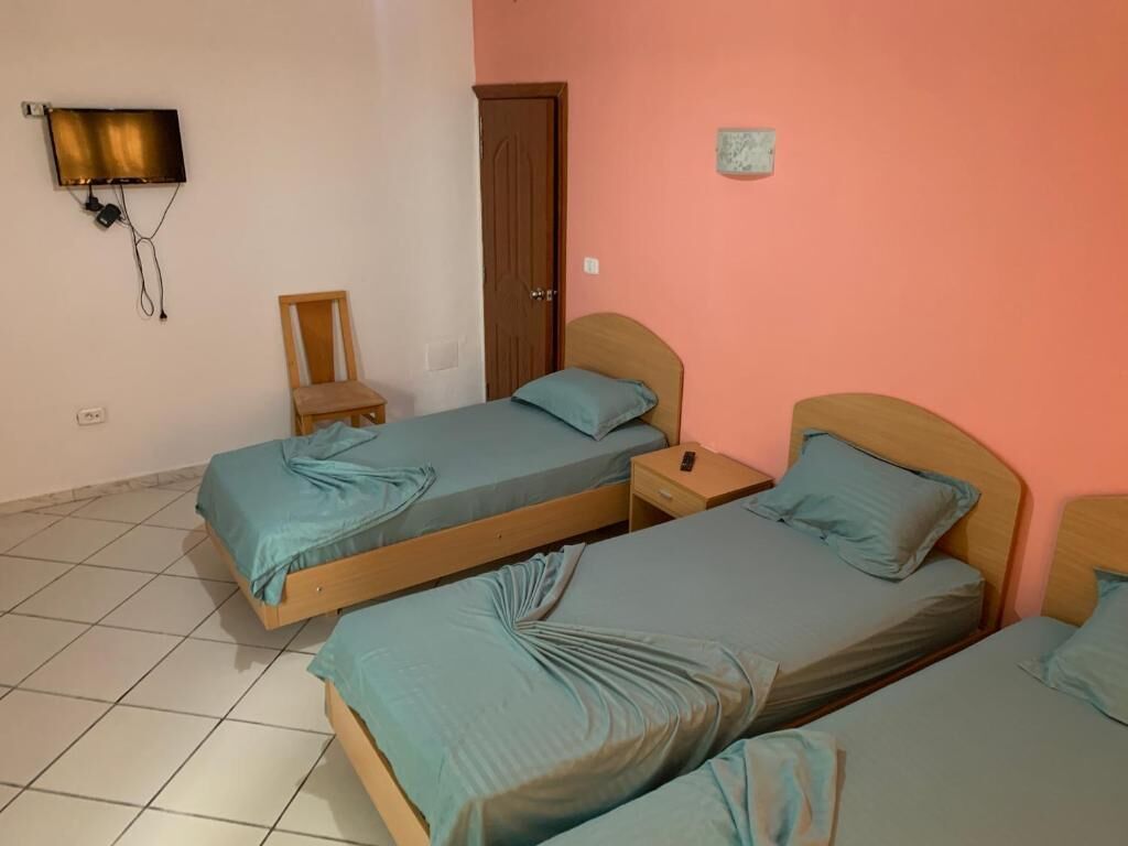 Una habitación con tres camas, un televisor montado en la pared, una silla de madera y una puerta.