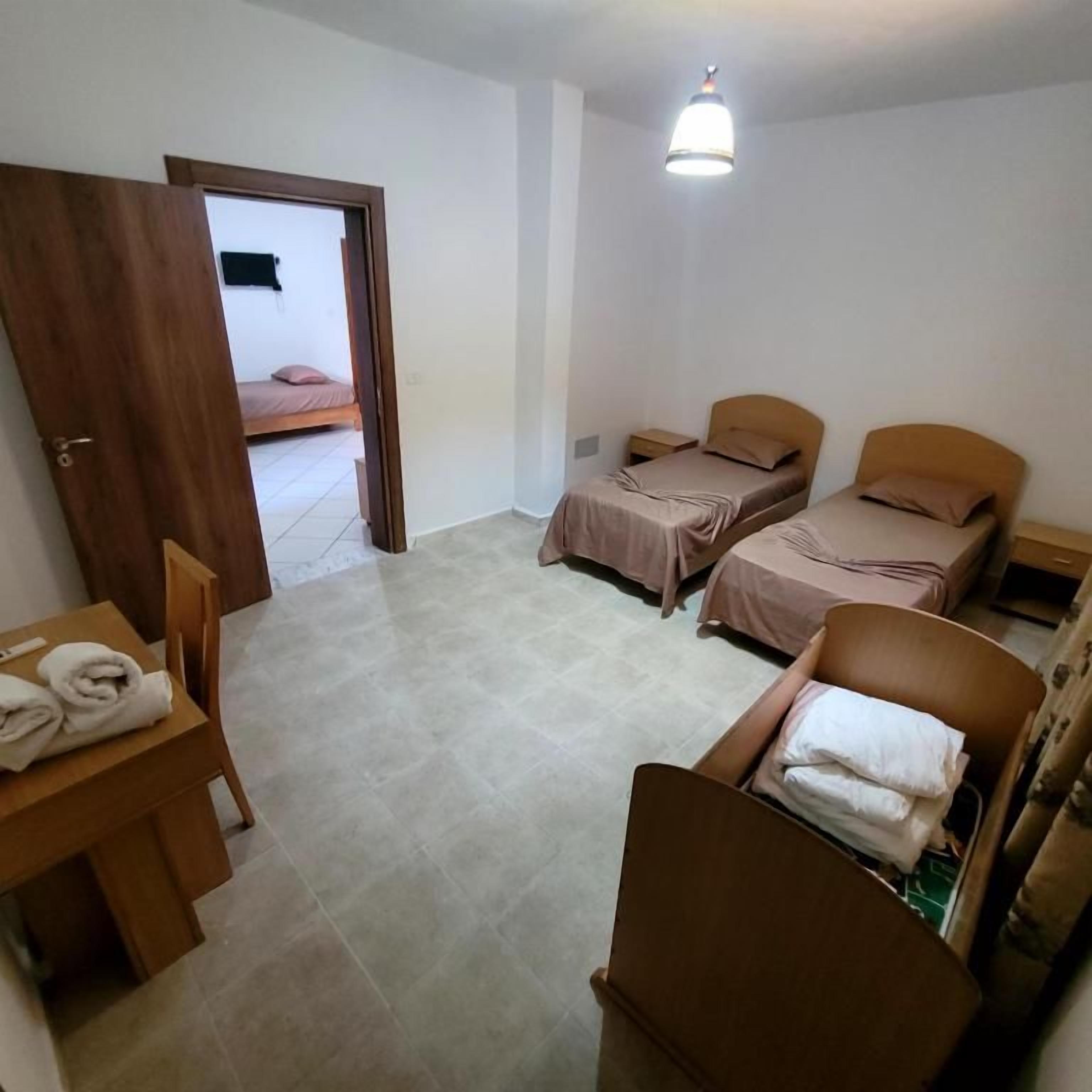 Una habitación pequeña y limpia con una cama, una silla, una mesa con toallas y una mesita de noche.
