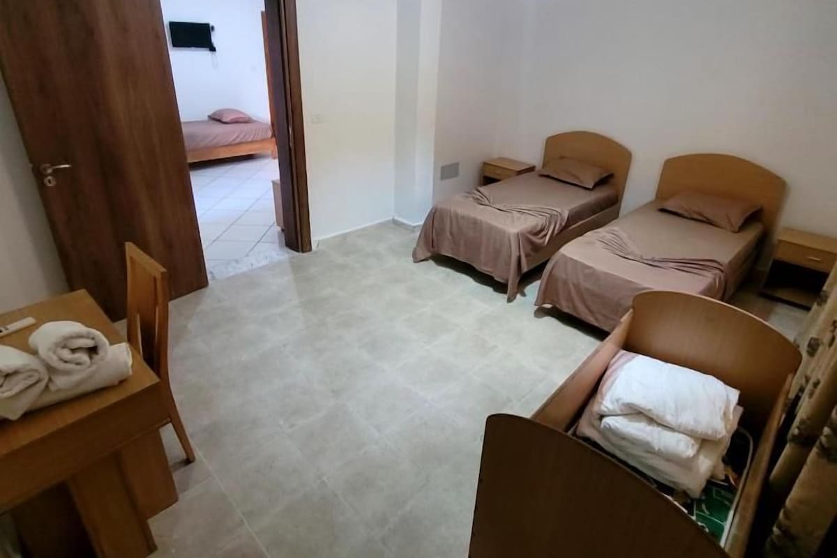 Una habitación pequeña y limpia con una cama, una silla, una mesa con toallas y una mesita de noche.