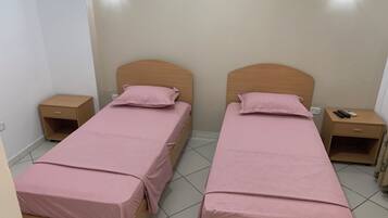 Quarto duplo com duas camas, cada uma com cabeceira de madeira, mesa de cabeceira e luminária na parede.