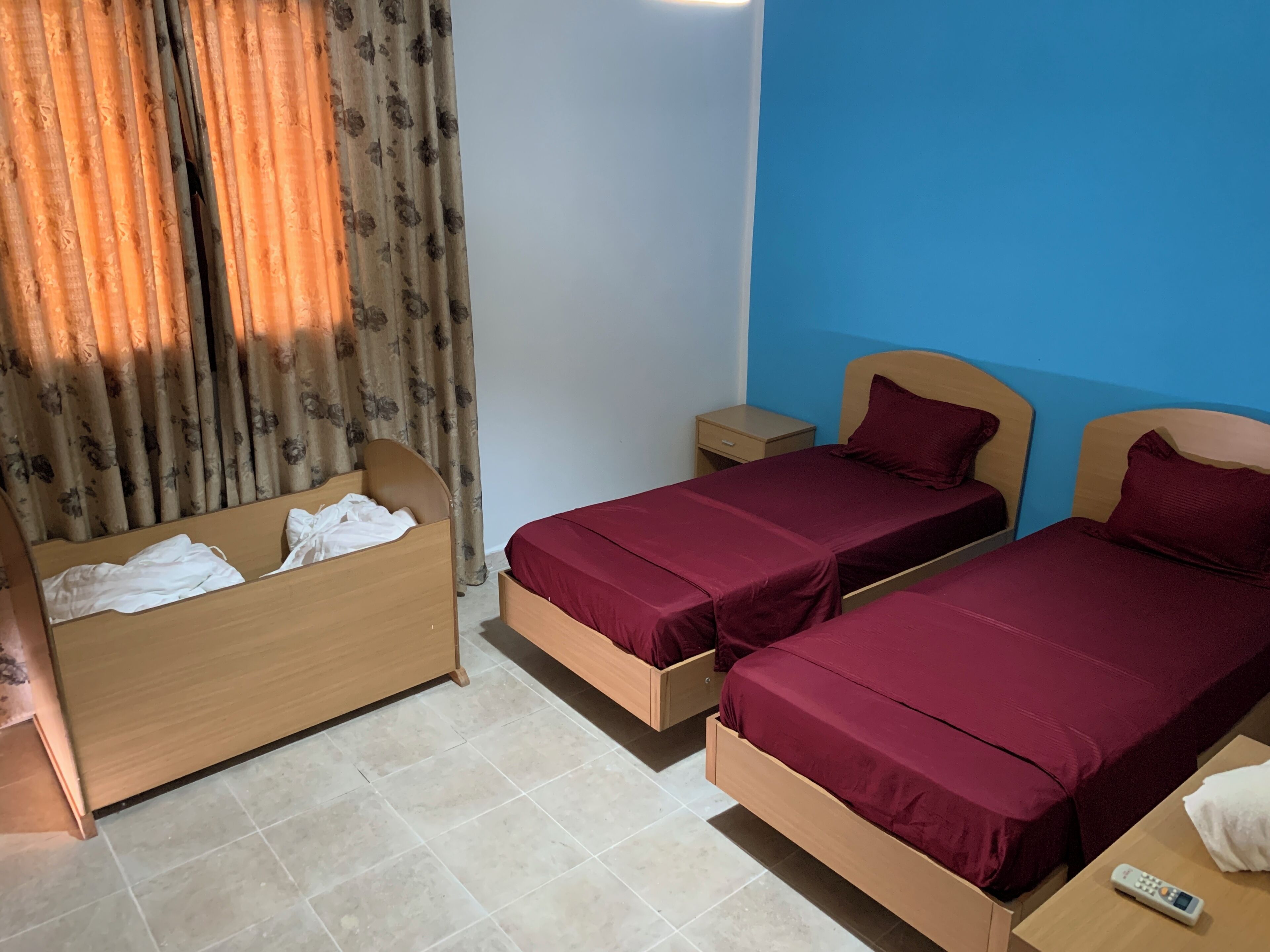 Une chambre avec deux lits, une table de chevet, un banc en bois et un rideau.