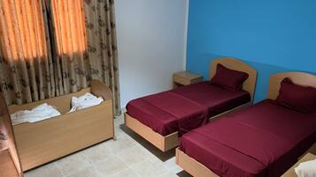 Une chambre avec deux lits, une table de chevet, un banc en bois et un rideau.
