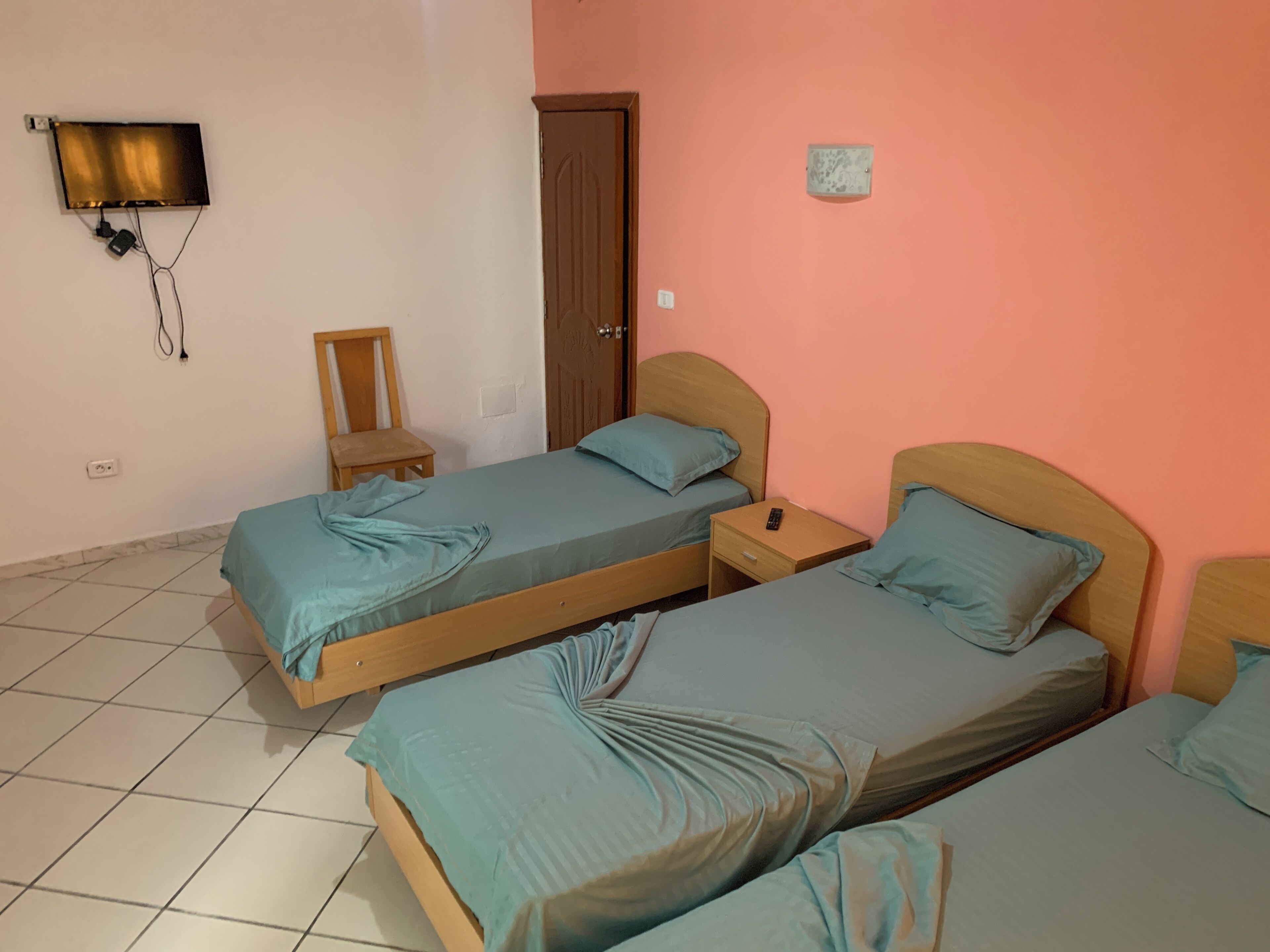 A bedroom with two beds, a wooden nightstand, a small table, a chair, a wardrobe, and a wall-mounted TV.