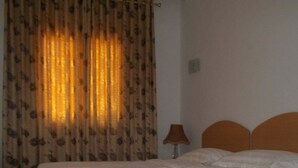Een bed met een witte spreideken, een lamp en een gordijn met een bloemenmotief.