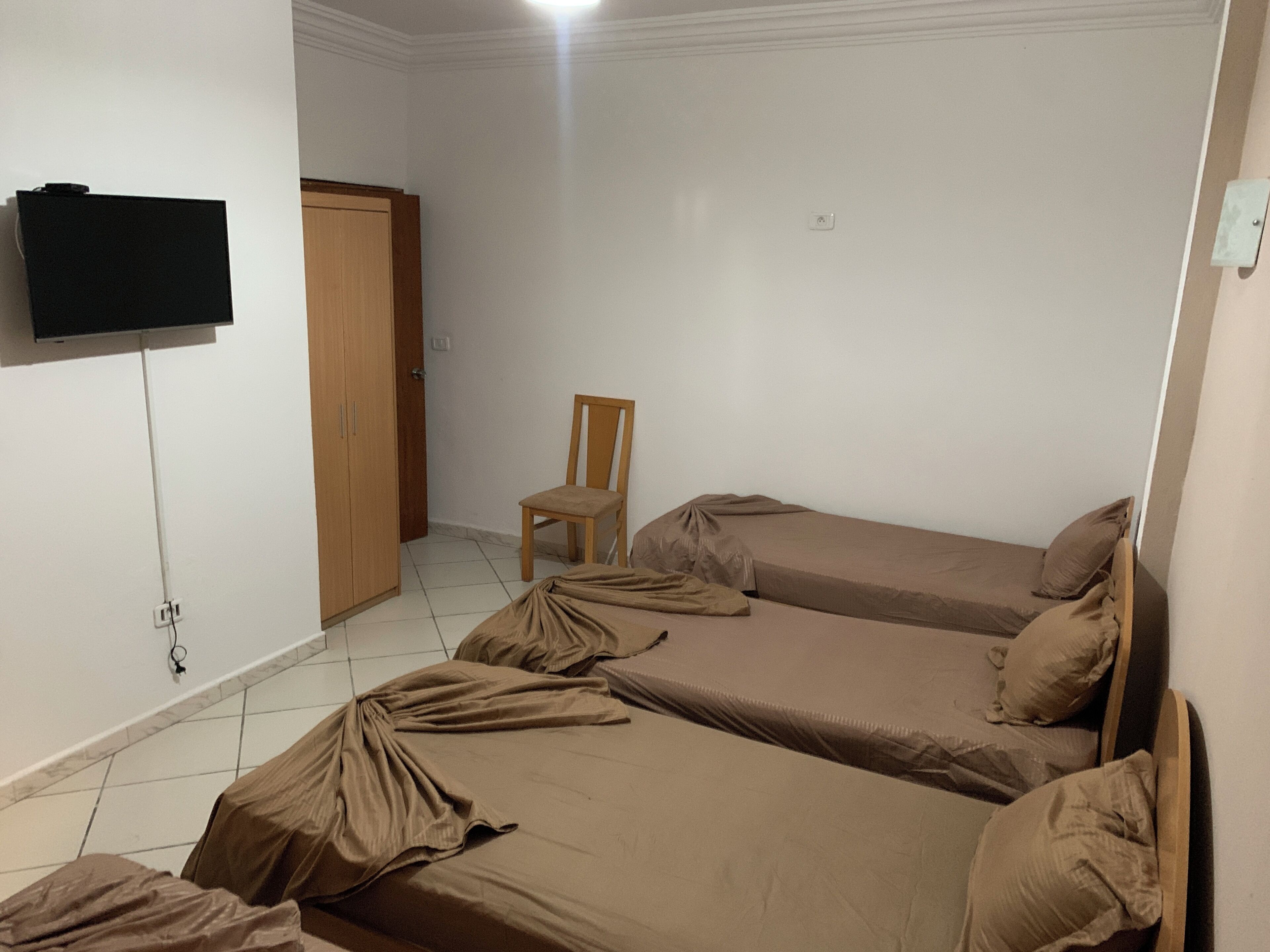 Una habitación con dos camas, una silla, un armario y un televisor fijado a la pared.