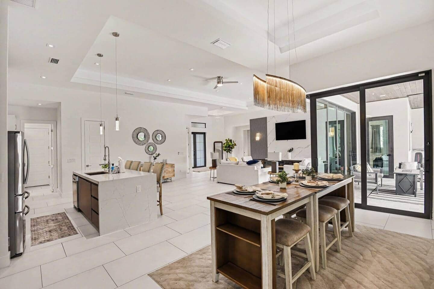 A modern kitchen with a central island, dining area with a wooden table, and a large sliding glass door leading to a balcony.