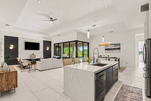 Una cucina moderna con isola centrale, una zona pranzo con divano e sedie, e un soggiorno con televisione e posti a sedere.
