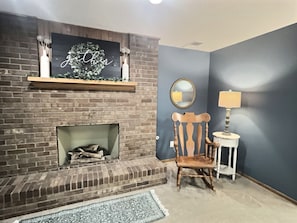 A brick fireplace with a mirror and a lamp on a side table, a wooden chair, and a rug on the floor. - Spacious, Big Family-Friendly 4 Bedroom Ranch Home in Hays, Kansas (Hays)