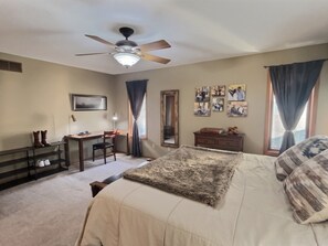 A bedroom with a bed, a desk, a chair, a ceiling fan, a mirror, and a window with curtains. - Spacious, Big Family-Friendly 4 Bedroom Ranch Home in Hays, Kansas (Hays)