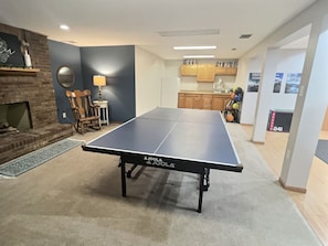 A ping pong table in a room with a fireplace, a dining table, and kitchen cabinets. - Spacious, Big Family-Friendly 4 Bedroom Ranch Home in Hays, Kansas (Hays)