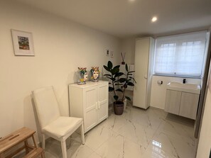 A small, clean room with a white chair, a cabinet, a potted plant, and a window with a view. - ENTIRE APARTMENT IN DOWNTOWN NAPLES (Napoli)