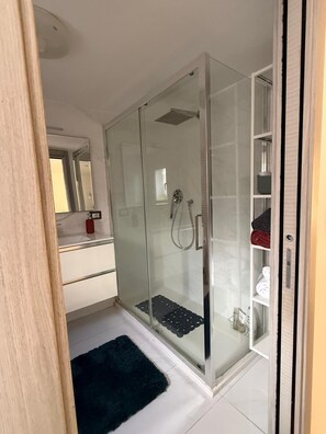 A modern bathroom with a glass-enclosed shower, a white sink, and a dark rug on the floor. - ENTIRE APARTMENT IN DOWNTOWN NAPLES (Napoli)
